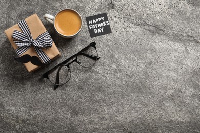 Photo of Card with phrase HAPPY FATHER'S DAY, gift box, eyeglasses and cup of aromatic coffee on grey background, flat lay. Space for text