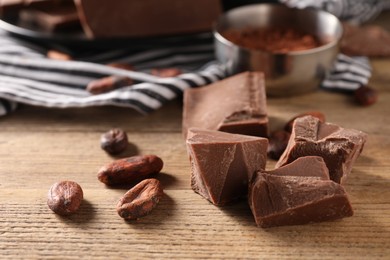 Photo of Pieces of tasty milk chocolate and cocoa beans on wooden table, closeup