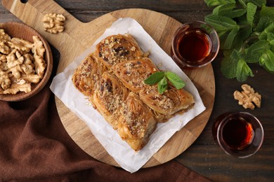 Photo of Eastern sweets. Pieces of tasty baklava, walnuts and tea on wooden table, flat lay