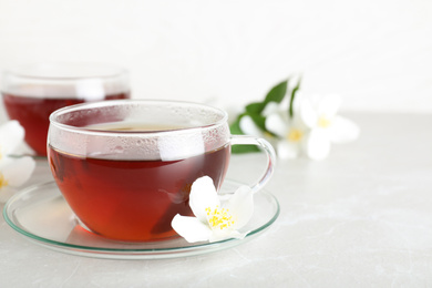 Photo of Cup of tea and fresh jasmine flower on light grey marble table