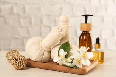 Photo of Beautiful jasmine flowers, herbal bags and skin care products on white wooden table