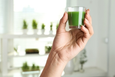 Photo of Woman holding shot glass of wheat grass juice indoors, closeup
