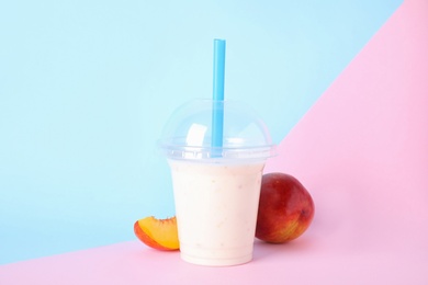 Photo of Tasty peach milk shake in plastic cup and fresh fruit on color background