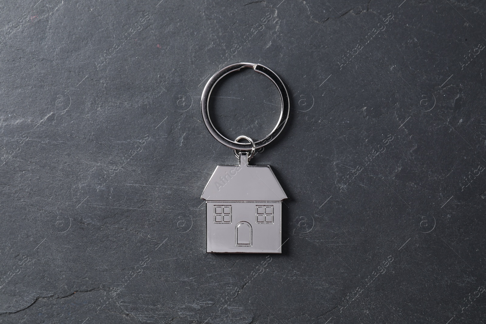 Photo of Metal keychain in shape of house on dark textured table, top view