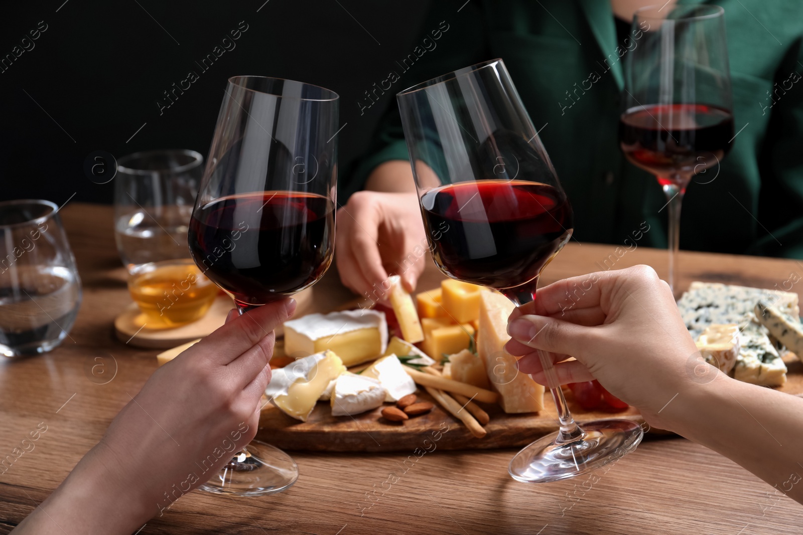 Photo of Women toasting with glasses of wine near cheese plate, closeup