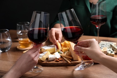 Photo of Women toasting with glasses of wine near cheese plate, closeup