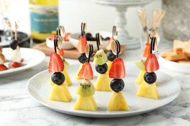 Tasty canapes with pineapple, kiwi and berries on white marble table, closeup