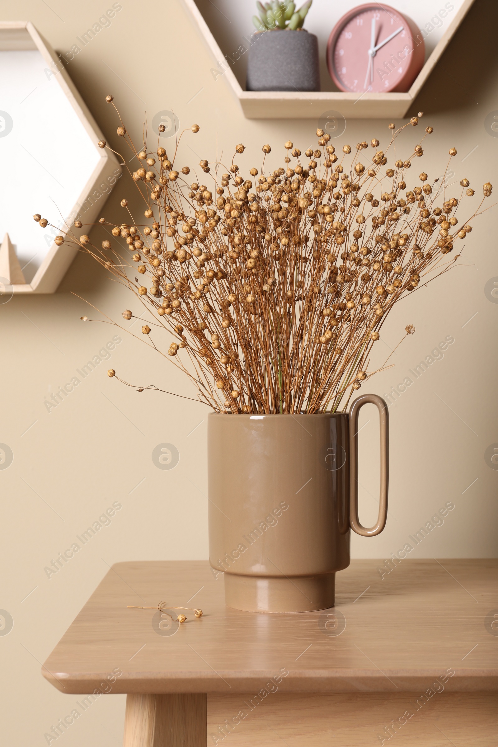 Photo of Stylish ceramic vase with dry flowers on wooden table near beige wall
