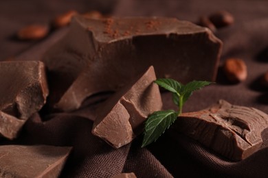 Photo of Pieces of tasty milk chocolate and mint on table, closeup