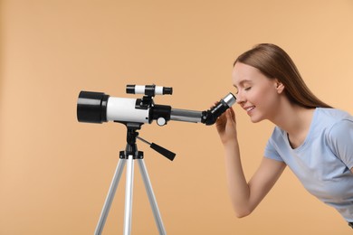Photo of Young astronomer looking at stars through telescope on beige background