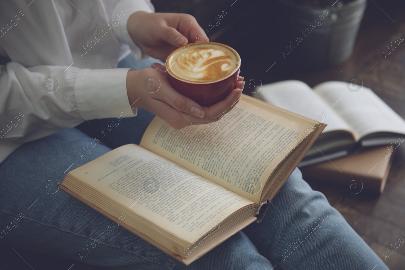 Image of Woman with cup of coffee reading book indoors, closeup