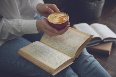 Image of Woman with cup of coffee reading book indoors, closeup