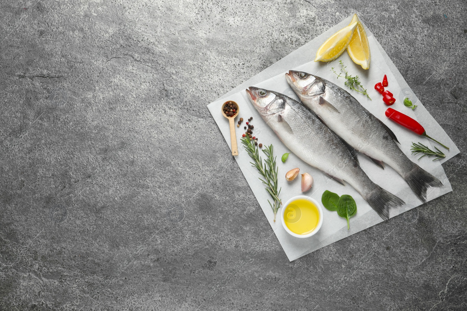 Photo of Sea bass fish and ingredients on grey table, top view. Space for text