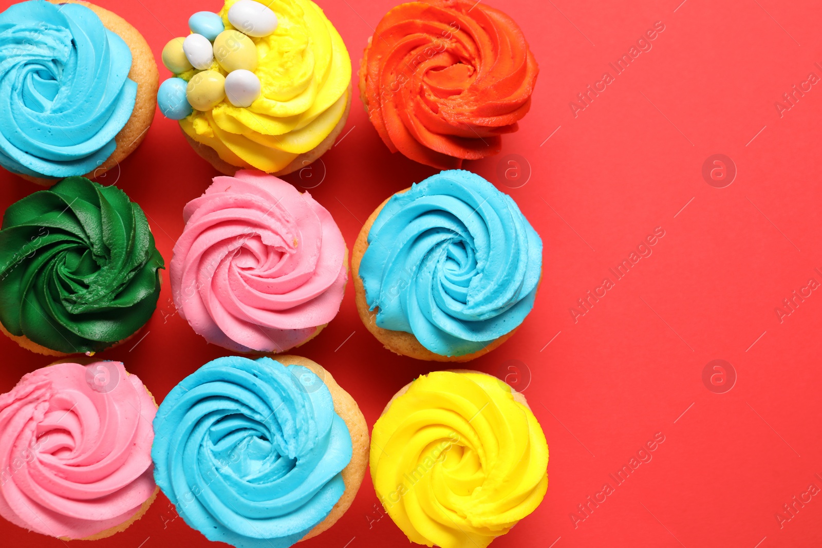 Photo of Delicious cupcakes with bright cream on red background, flat lay. Space for text