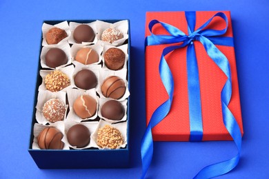 Photo of Box with delicious chocolate candies on blue background, closeup