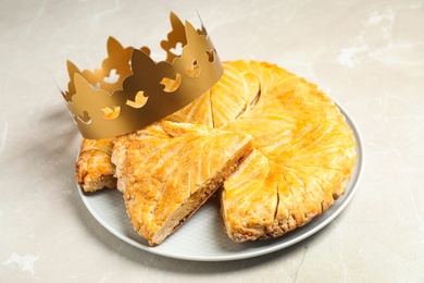 Photo of Traditional galette des Rois with paper crown on light grey marble table