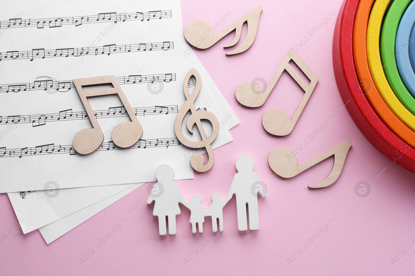 Photo of Baby songs. Music sheets, figures of family, wooden notes and toy rainbow on pink background, flat lay