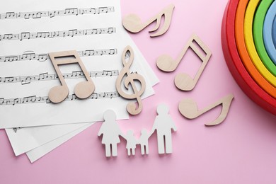 Photo of Baby songs. Music sheets, figures of family, wooden notes and toy rainbow on pink background, flat lay