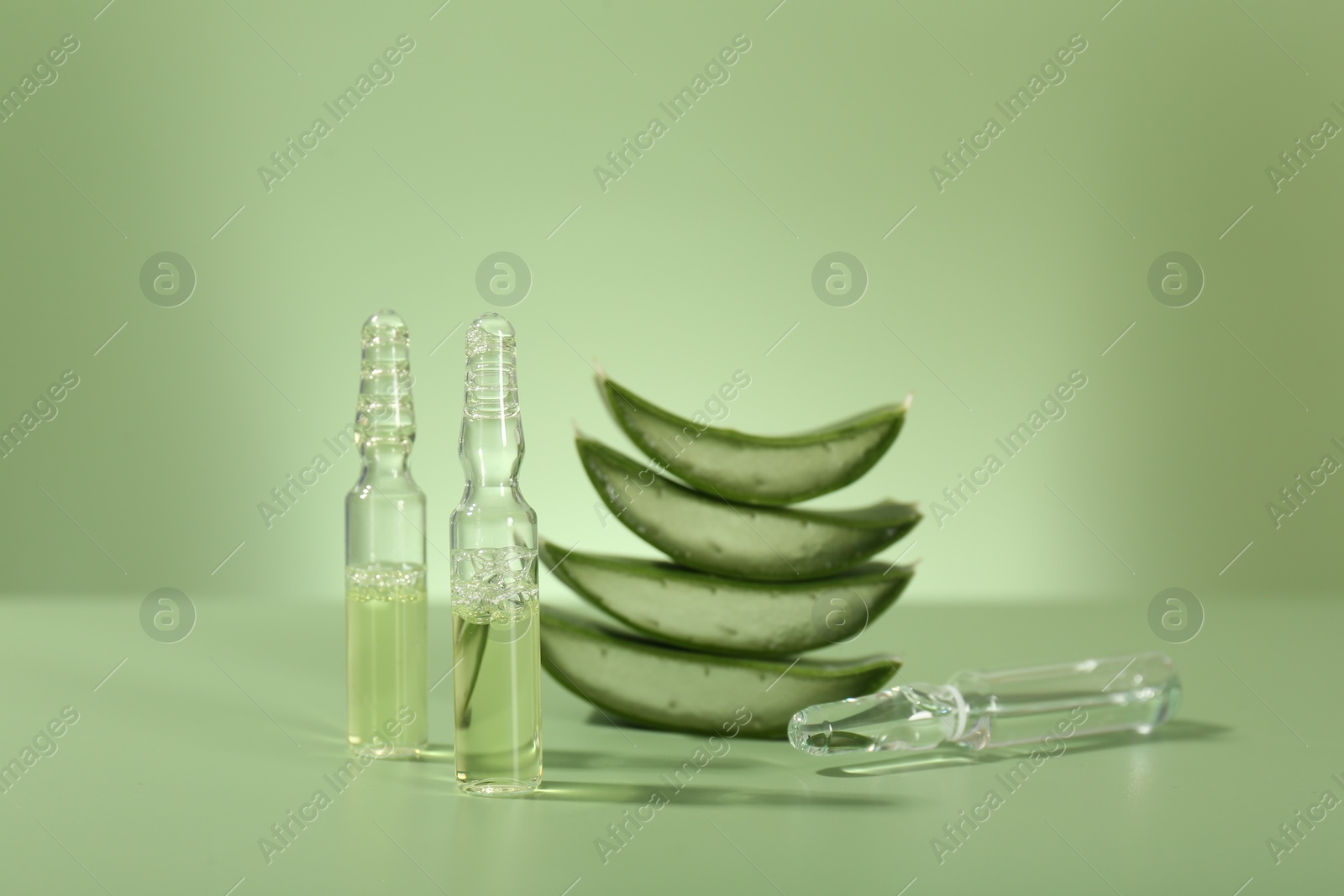 Photo of Skincare ampoules with extract of aloe vera and cut leaves on pale green background