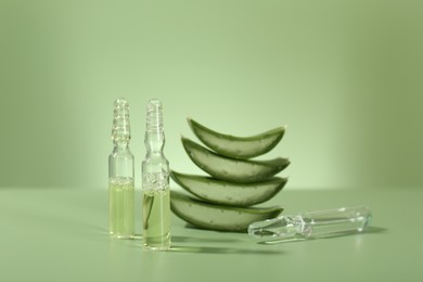 Skincare ampoules with extract of aloe vera and cut leaves on pale green background