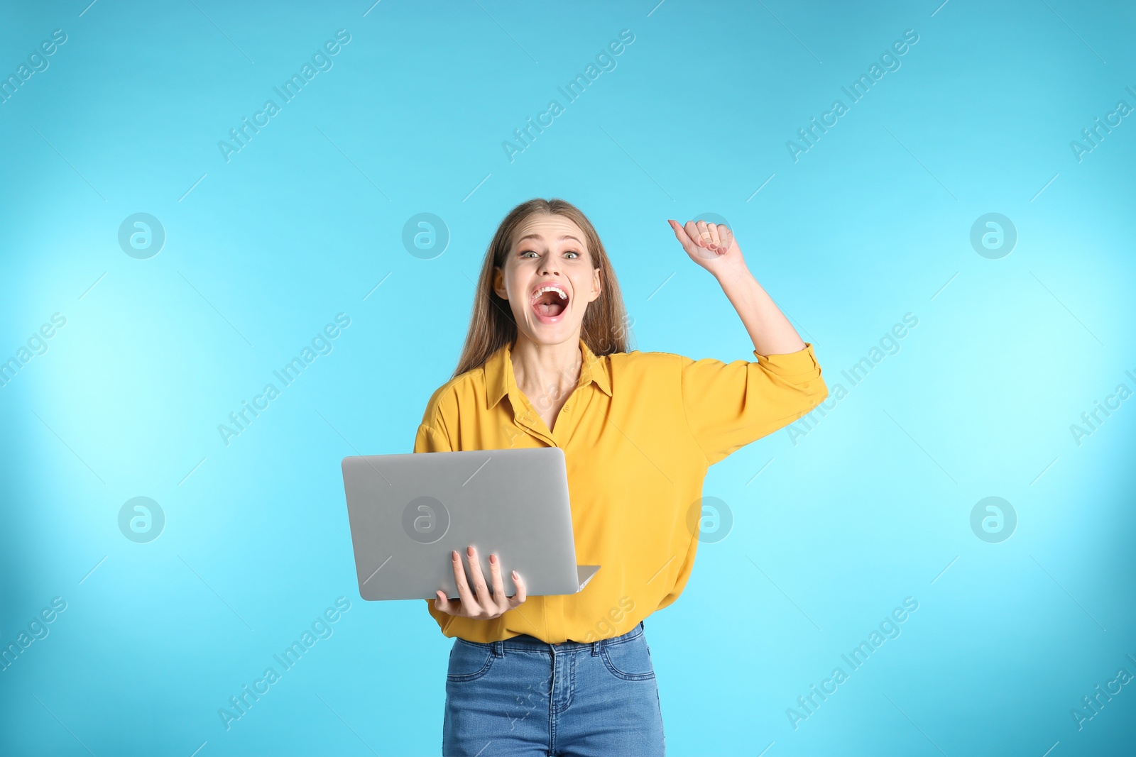 Photo of Emotional young woman with laptop celebrating victory on color background