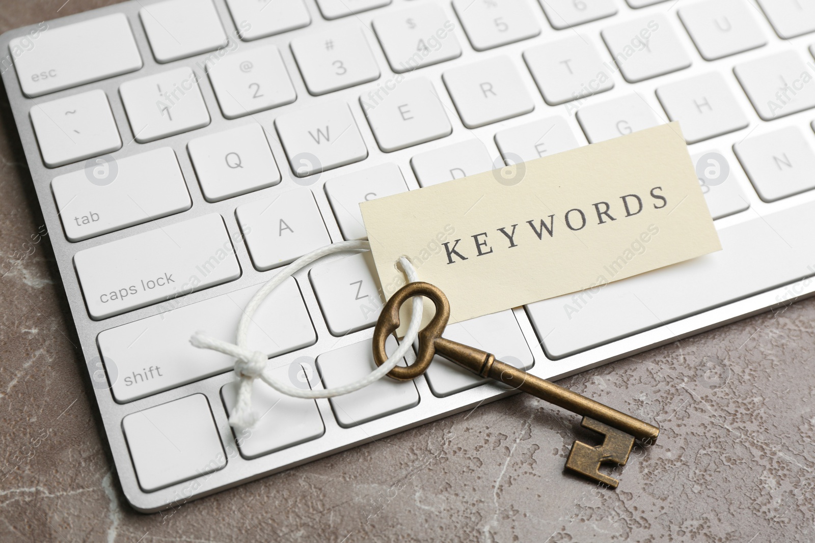 Photo of Keyboard, vintage key and tag with word KEYWORDS on grey table, closeup