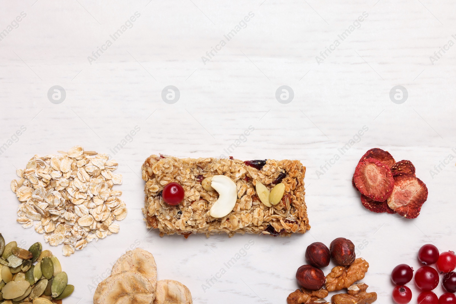 Photo of Tasty granola bar and ingredients on white wooden table, flat lay. Space for text