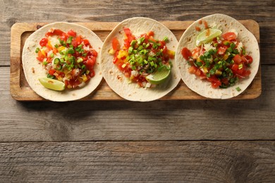 Photo of Delicious tacos with vegetables, green onion, lime and ketchup on wooden table, top view. Space for text