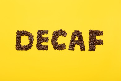 Photo of Word Decaf made of coffee beans on yellow background, flat lay
