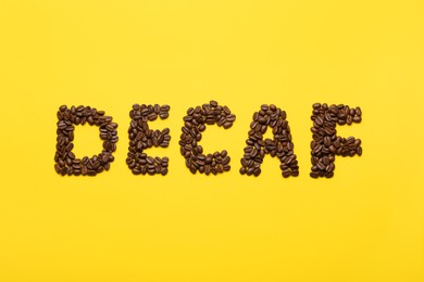 Word Decaf made of coffee beans on yellow background, flat lay