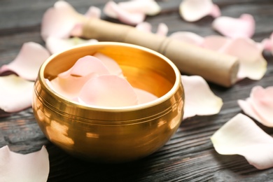 Photo of Golden singing bowl and petals on black wooden table, closeup. Sound healing