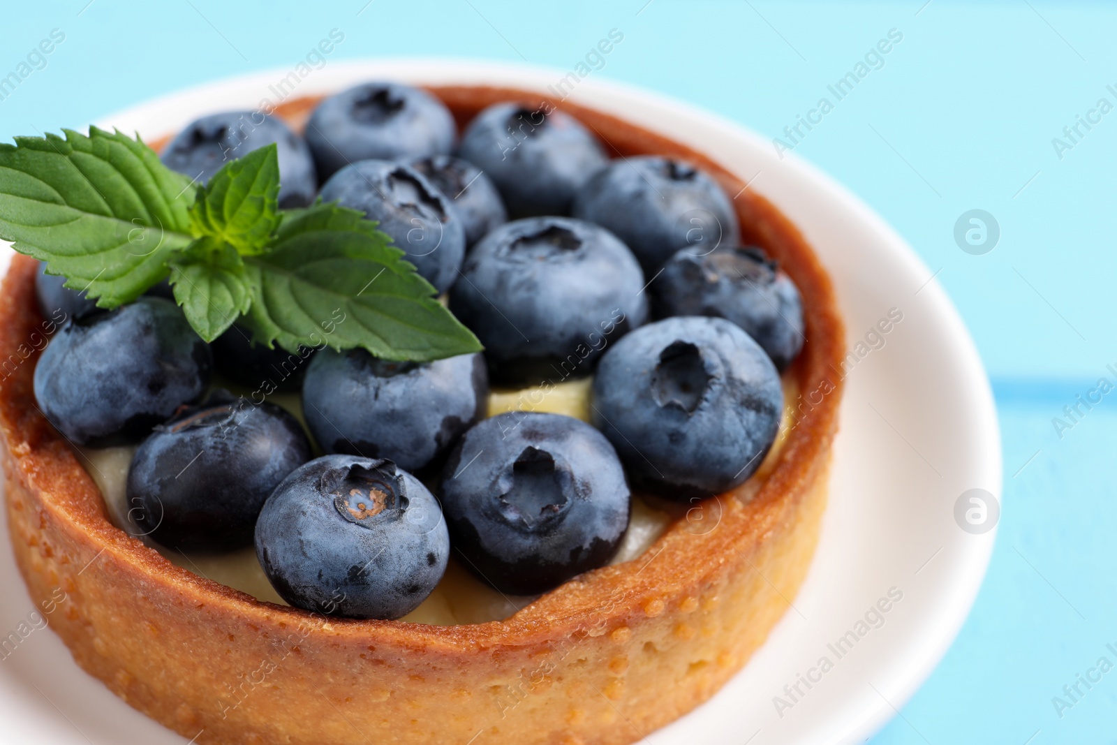 Photo of Tartlet with fresh blueberries on light blue table, closeup. Delicious dessert