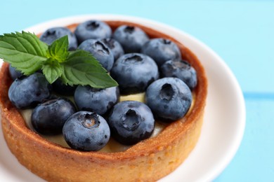 Photo of Tartlet with fresh blueberries on light blue table, closeup. Delicious dessert