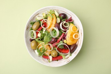 Photo of Bowl of tasty salad with leek and olives on light green table, top view