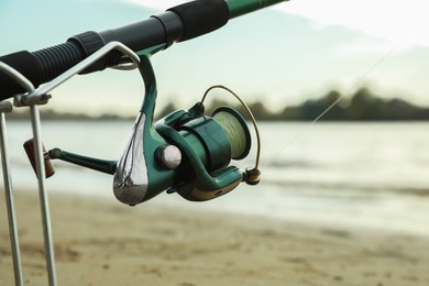 Photo of Fishing rod with reel on sand near river, closeup. Space for text