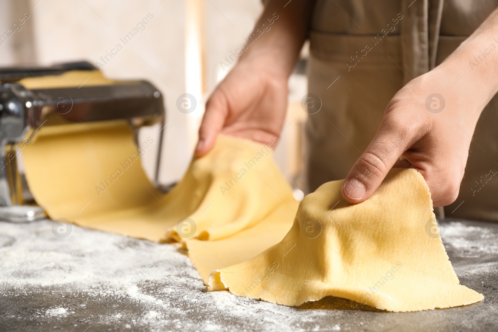 Photo of Woman preparing dough with pasta maker machine at grey table, closeup