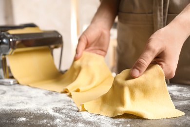 Woman preparing dough with pasta maker machine at grey table, closeup