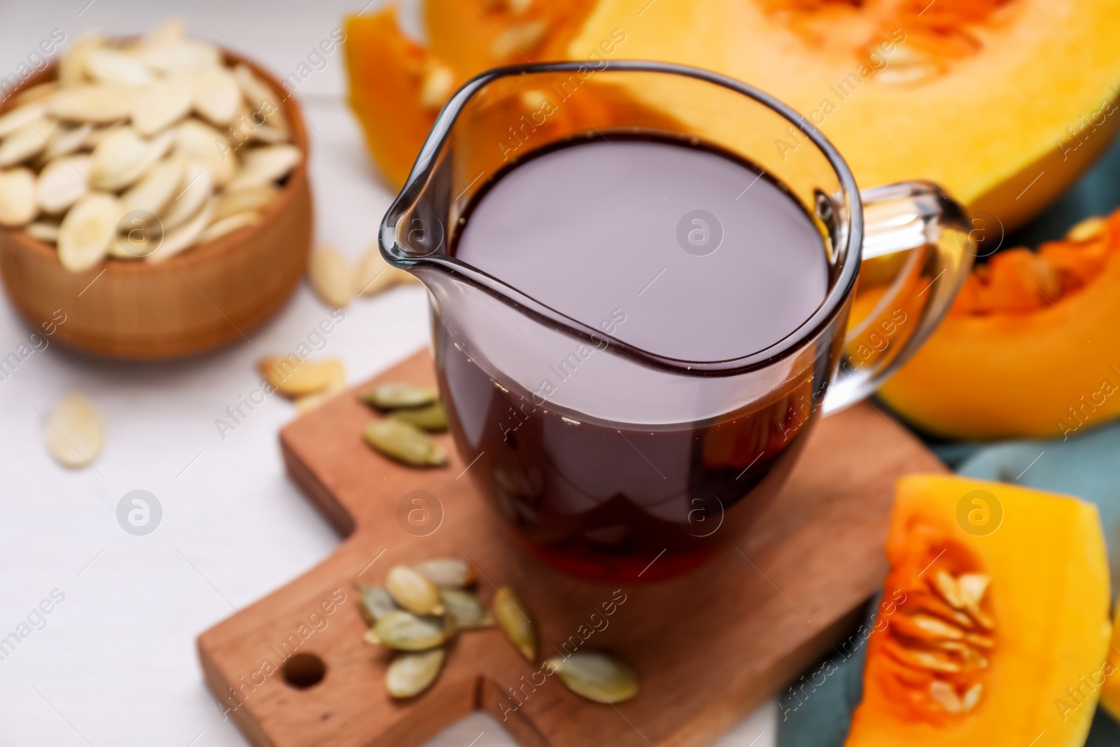 Photo of Fresh pumpkin seed oil in glass pitcher on white wooden table