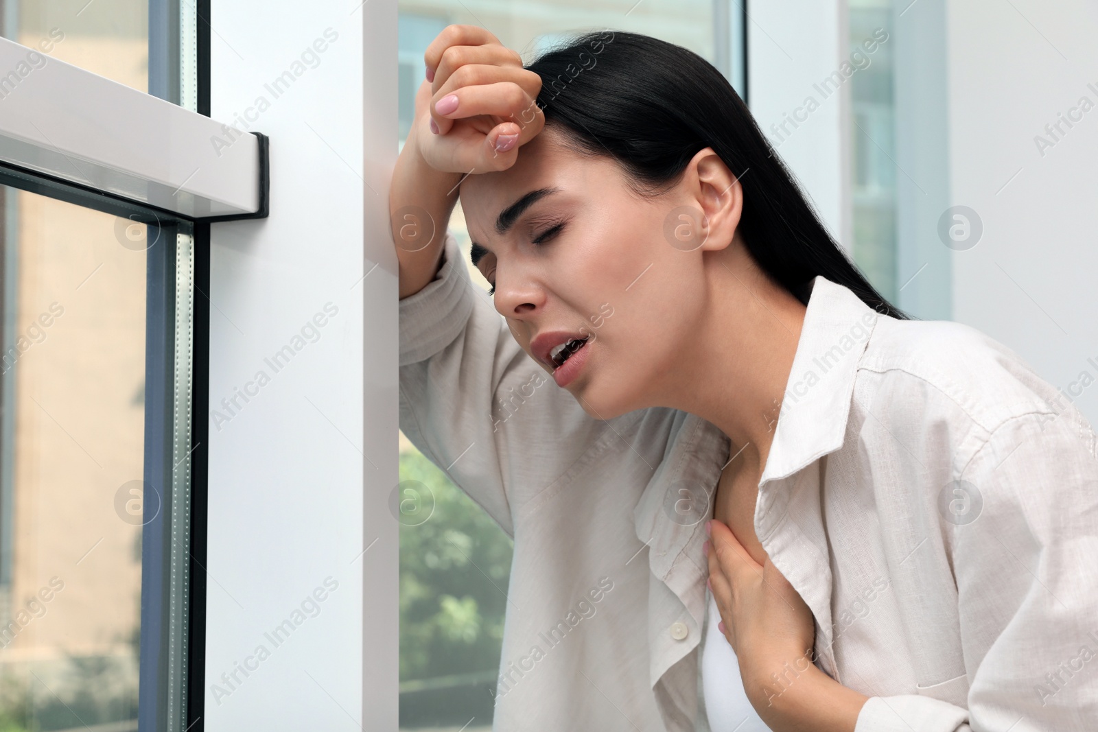 Photo of Young woman suffering from breathing problem near window indoors