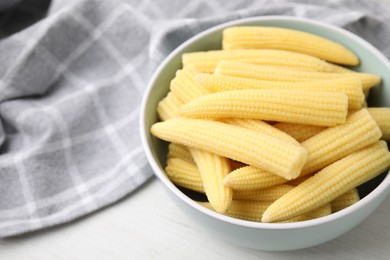 Photo of Tasty fresh yellow baby corns in bowl on white wooden table, closeup. Space for text