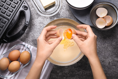 Photo of Woman preparing dough for Belgian waffles at grey table, top view