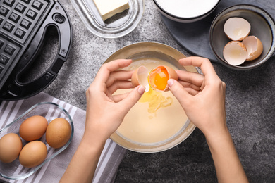 Woman preparing dough for Belgian waffles at grey table, top view