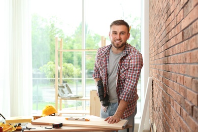 Photo of Young man working with electric screwdriver near brick wall. Space for text