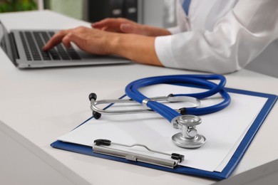 Doctor during patient consultation, clipboard and stethoscope on white table in clinic, closeup