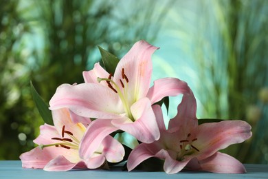 Photo of Beautiful pink lily flowers on turquoise table against blurred green background