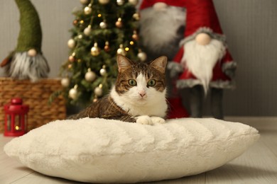 Photo of Cute cat lying on soft pillow near Christmas decor at home. Adorable pet