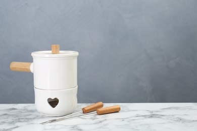 Photo of Fondue set on white marble table against light grey background, space for text