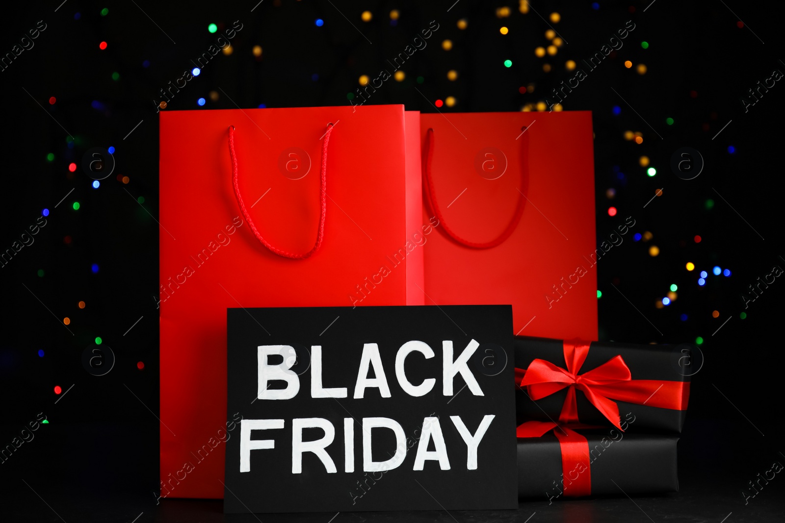 Photo of Paper shopping bags, gift boxes and phrase Black Friday against blurred lights