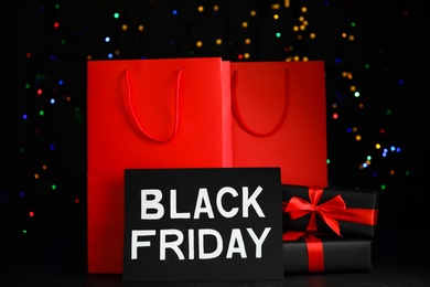 Photo of Paper shopping bags, gift boxes and phrase Black Friday against blurred lights