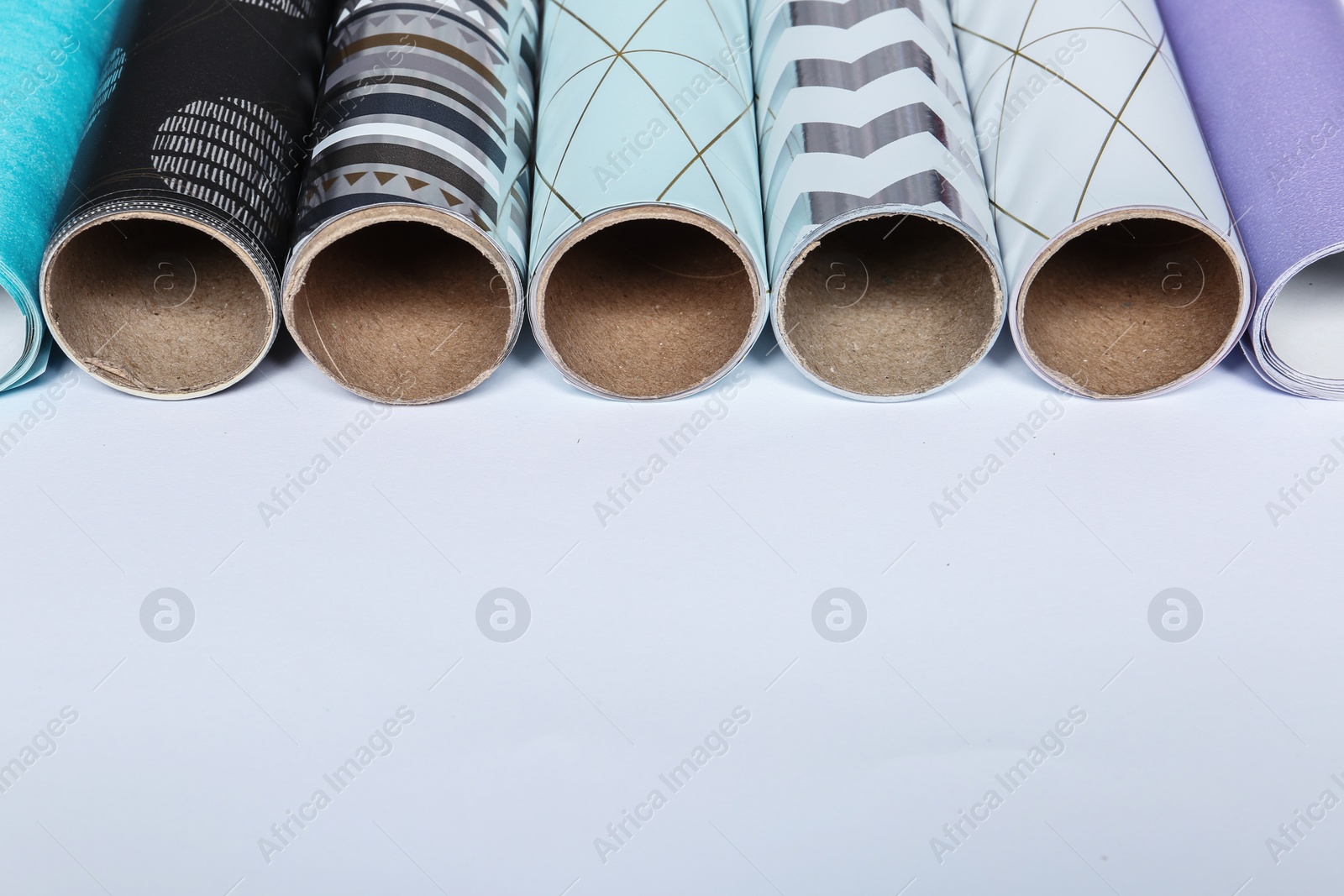 Photo of Rolls of festive wrapping paper and space for text on white background, closeup. Gift box packaging ideas